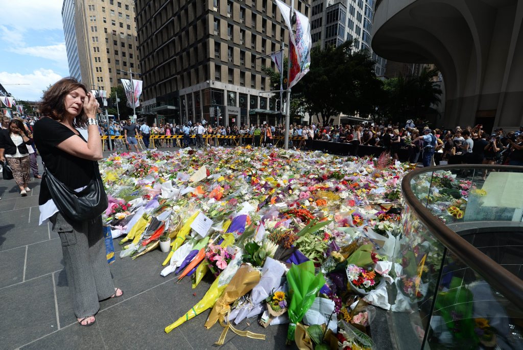 A visitor looks at a makeshift memorial near the scene of a fatal siege in the heart of Sydney's financial district on December 16, 2014. Sydneysiders including tearful office workers and Muslim women in hijabs laid flowers at the scene of the deadly siege, in an outpouring of grief and shock that this could happen in their easy-going city. AFP PHOTO/Peter PARKS A visitor looks at a makeshift memorial near the scene of a fatal siege in the heart of Sydney's financial district on December 16, 2014. Sydneysiders including tearful office workers and Muslim women in hijabs laid flowers at the scene of the deadly siege, in an outpouring of grief and shock that this could happen in their easy-going city. AFP PHOTO/Peter PARKS